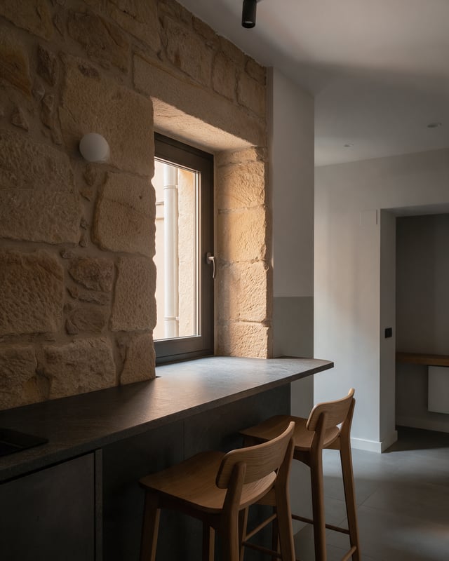 Rincón de cocina reformada con pared de piedra, barra de piedra oscura y taburetes de roble